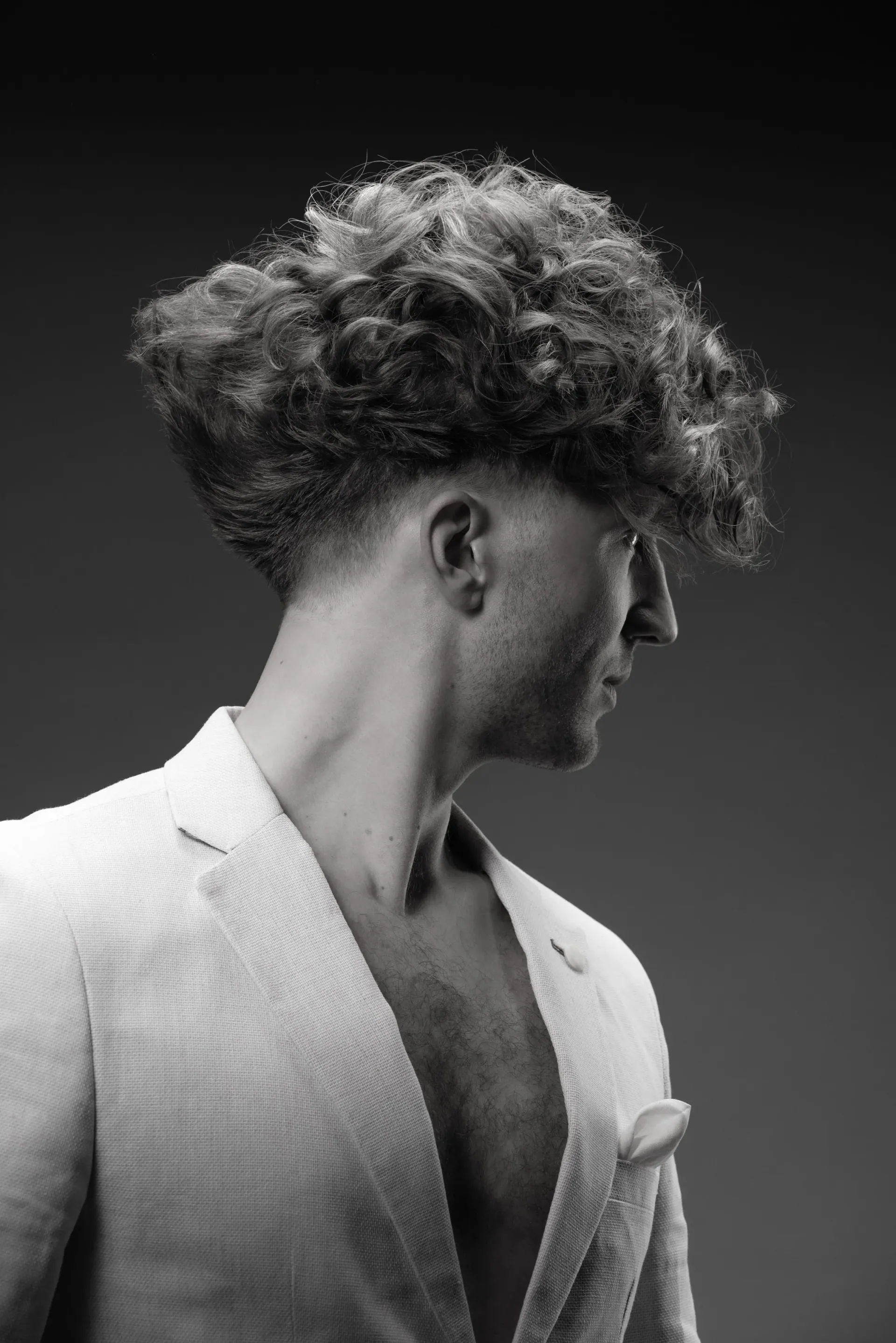 Black-and-white photograph of a man in profile with large curly hair and an open white blazer